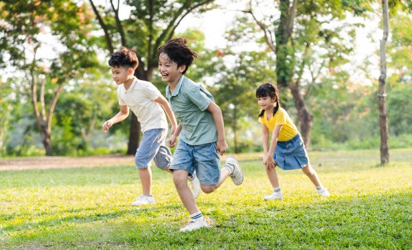 Three kids play outdoors on grass and under the sun.