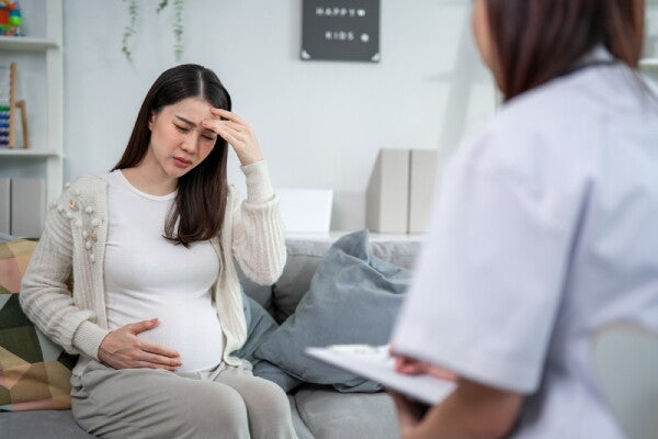 32-week-pregnant Asian with one hand in her forehead and the other on her belly consults a doctor