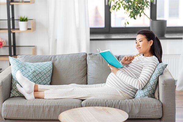 A 33 weeks pregnant Asian sitting on the sofa and making a list of things to prepare before birth.