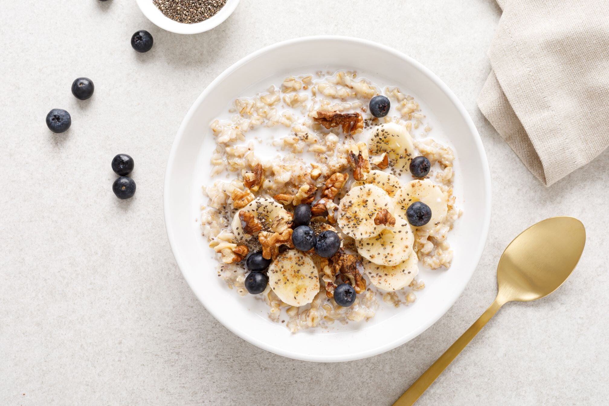 A bowl of oat porridge made with almond milk and topped with bananas, blueberries, walnuts and chia seeds