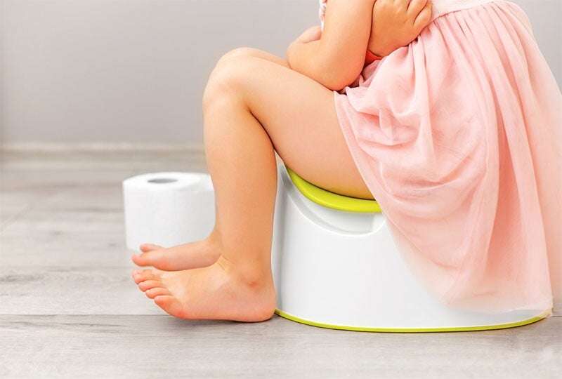 A female toddler holds her stomach as she sits on the potty