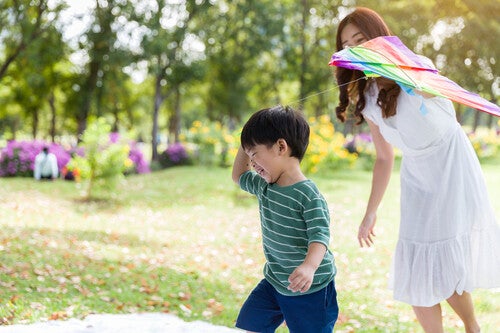 A happy Asian preschooler boy running and playing with a kite in the park with his mom