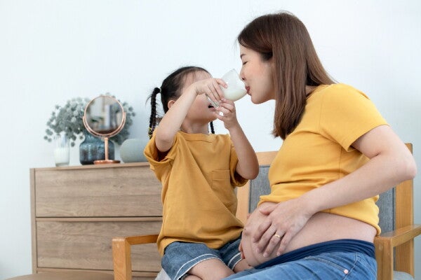 A little Asian girl giving her pregnant mom a sip of milk from a glass at home