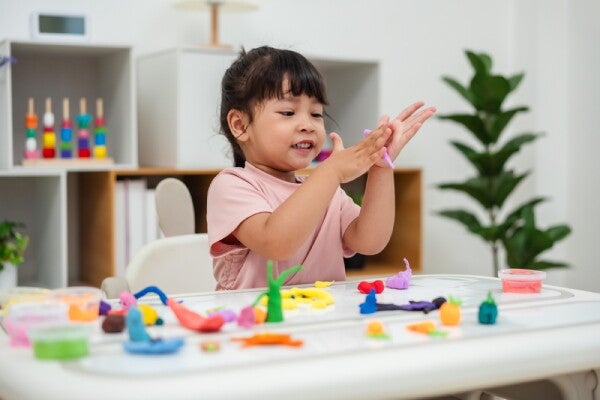 A little Asian girl playing with clay at home, alone.
