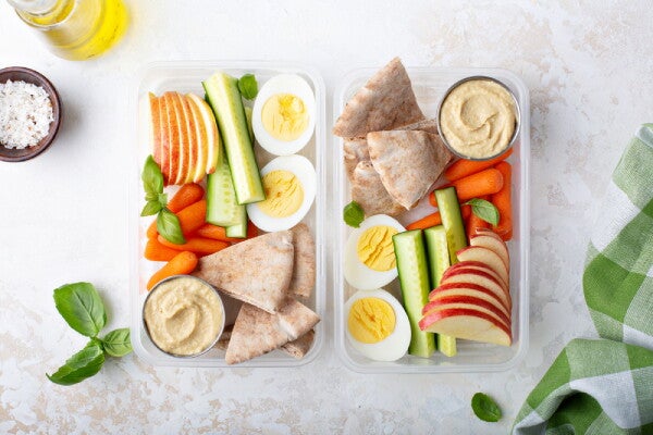 A lunchbox containing hummus and pita, eggs, and vegetables as healthy snacks for kids.