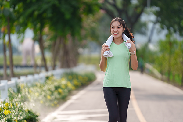 A young Asian woman in workout wear walking briskly in the park in the morning.