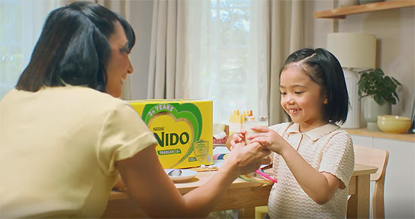 A mother and her young child sharing a happy moment at home while preparing a glass of NIDO®, showing daily nutrition and loving care for a growing child.
