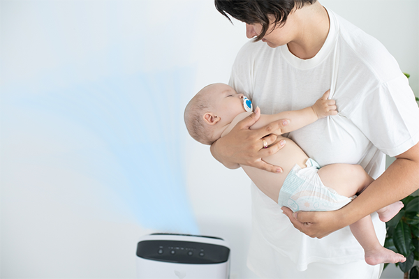 A mother carrying her sleeping baby near an air purifier at home.