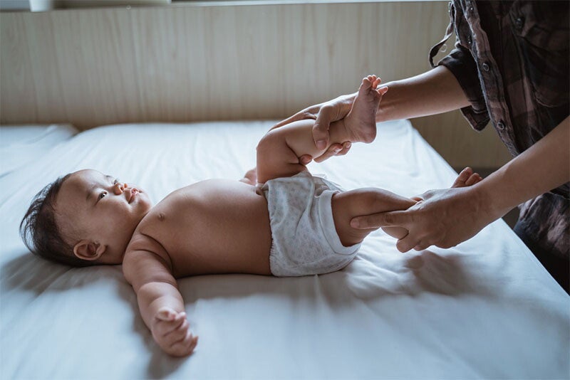 A parent holds her baby's legs to move them in cycling motion for baby constipation relief