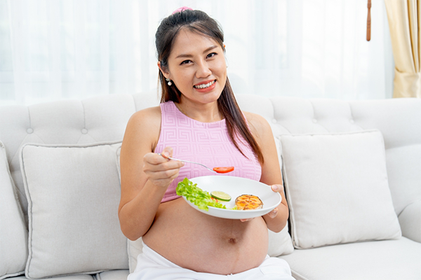 A pregnant Asian woman eating a salad and salmon at home.