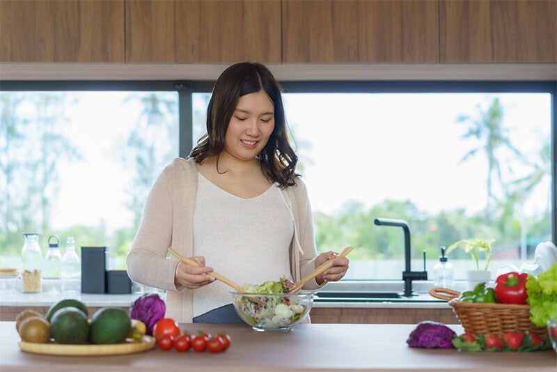 A pregnant Asian woman preparing a vegetable salad in her home kitchen