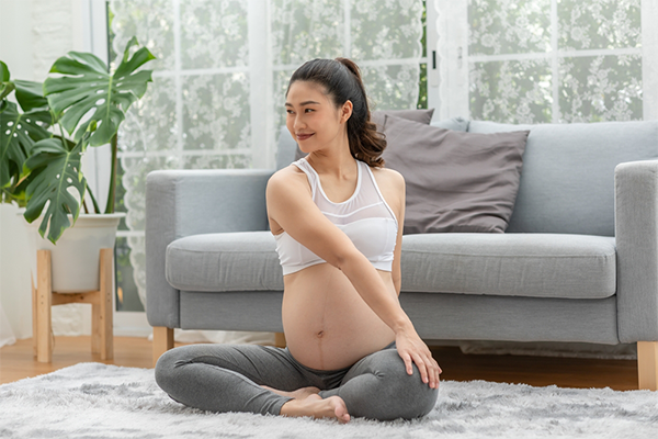 A pregnant Asian woman sitting on a yoga mat and stretching.