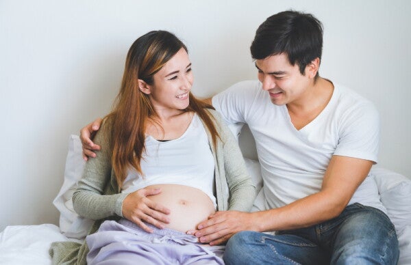 A pregnant Asian woman with her husband sitting in bed at home and talking.