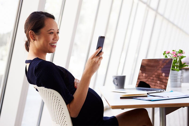 A pregnant businesswoman reading a text message in a cafe.