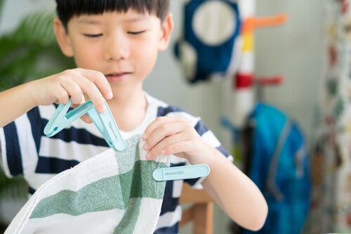 A preschool boy concentrates using colored clothes pegs to clip onto a colored kitchen cloth