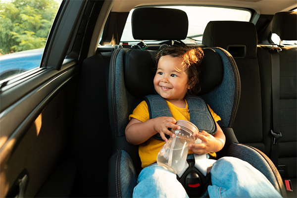 A smiling Asian little girl securely sitting in a front-facing car seat.