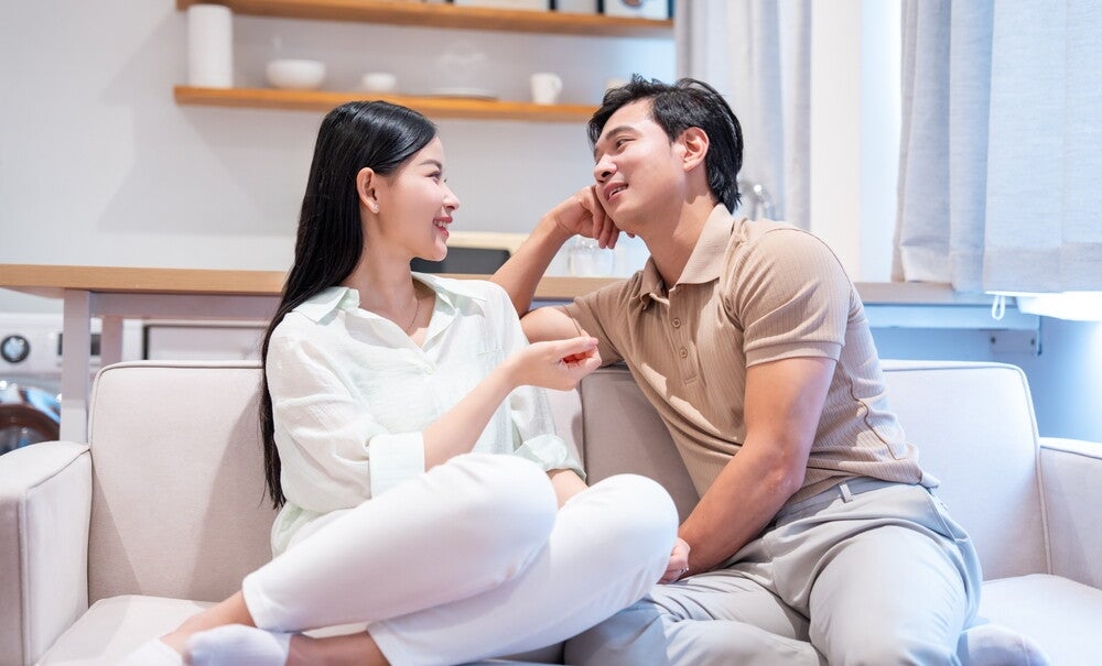 A young Asian couple seated on the sofa and discussing the pros and cons of different natural family planning methods