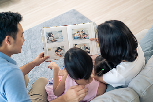 A young Asian couple showing their two little girls a family photo album