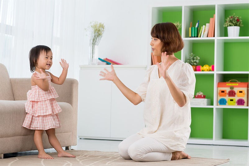 A young Asian girl singing a Filipino nursery rhyme with her mother at home.