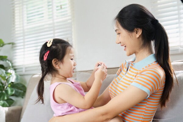 A young Asian mom actively listening to her little girl at home in the living room.