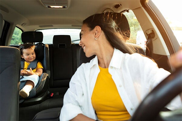 A young Asian mom smiling at her toddler daughter in a front-facing car seat