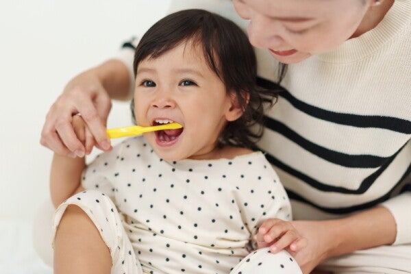 A young Asian mother helping her child brush her teeth to prevent tooth decay in kids