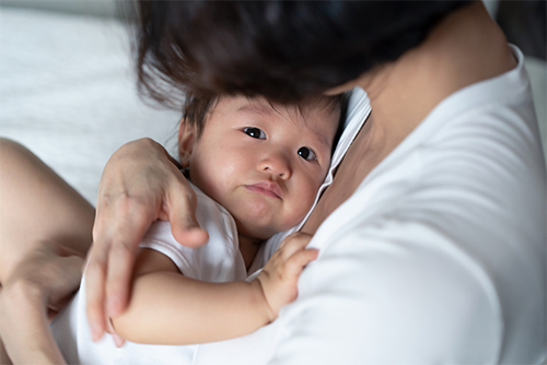 A young Asian mother hugging and holding her crying baby in her arms