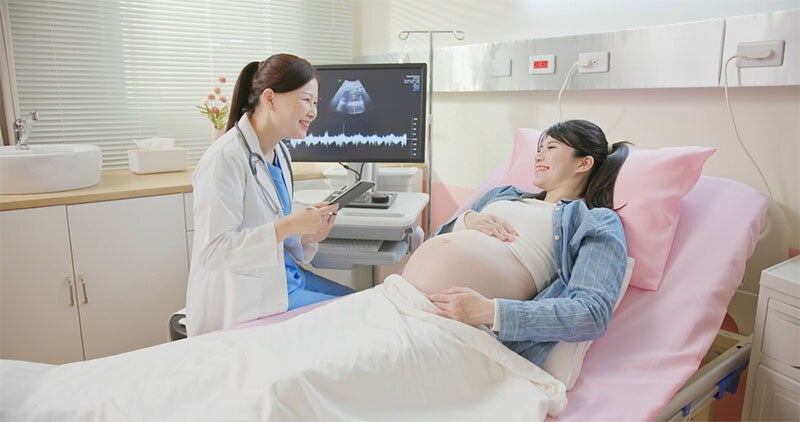 : A young asian pregnant woman lying in hospital bed and talking to the doctor about her signs of labor