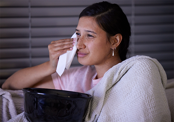 A young emotional woman wiping away a tear while watching a movie at home