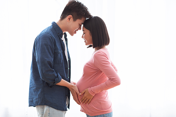 A young pregnant Asian couple feeling their baby’s first kicks.
