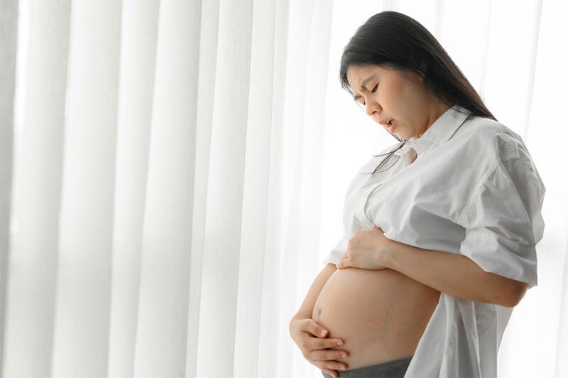 : A young pregnant Asian woman standing and touching her belly
