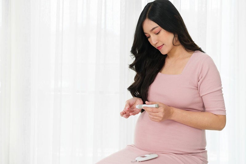 A young pregnant woman holding a glucose meter and checking her blood sugar level at home