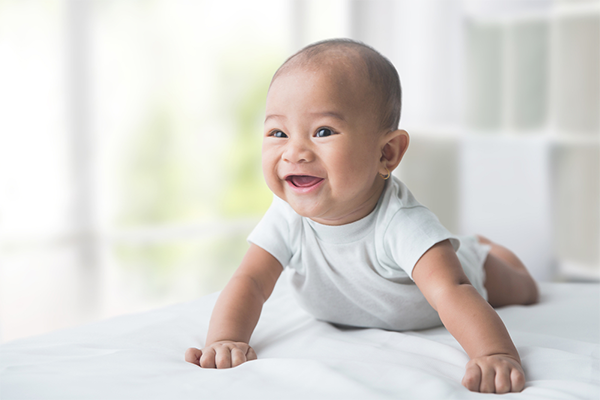 Adorable Asian baby push up onto their forearms, a key motor skill, during tummy time