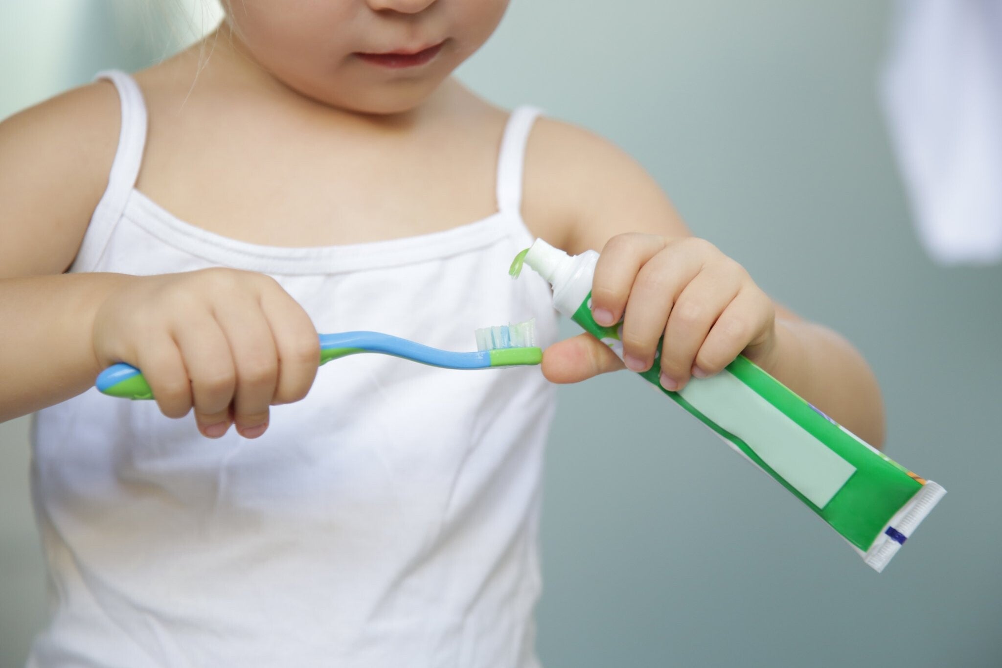  A 3-year-old girl squeezing out toothpaste onto a toothbrush in the bathroom. 