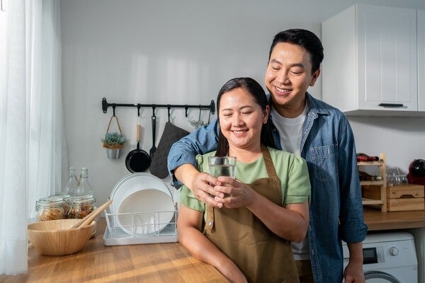 An Asian man giving his wife a glass of water in the kitchen at home