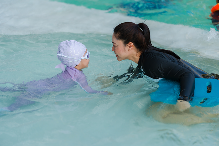 An Asian preschooler girl learning to swim with her mom in a pool.