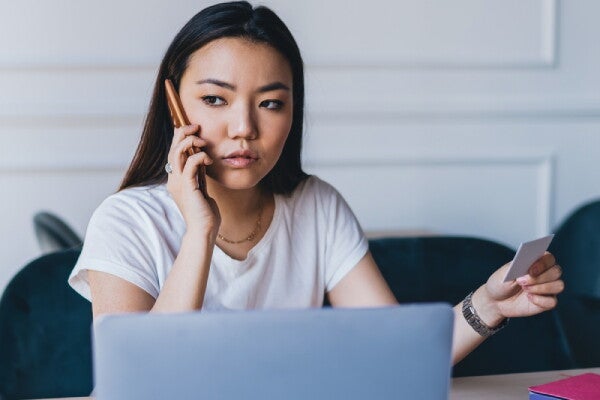 An Asian woman on the phone while holding her ID to ask how to renew it.