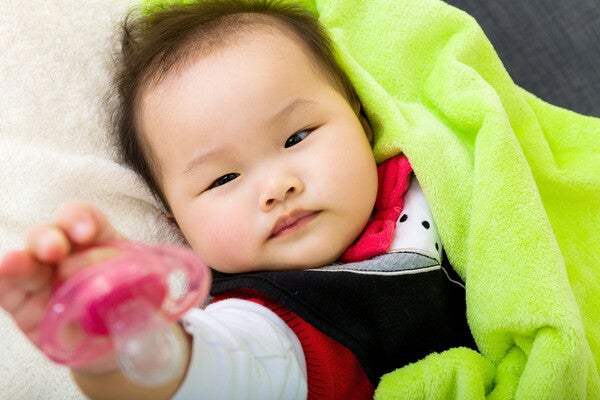 Asian baby lying down and giving pacifier back.