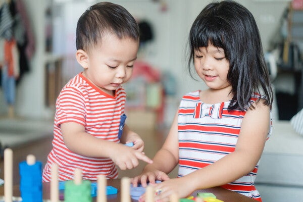 Asian girl shares her toy with her younger brother. 