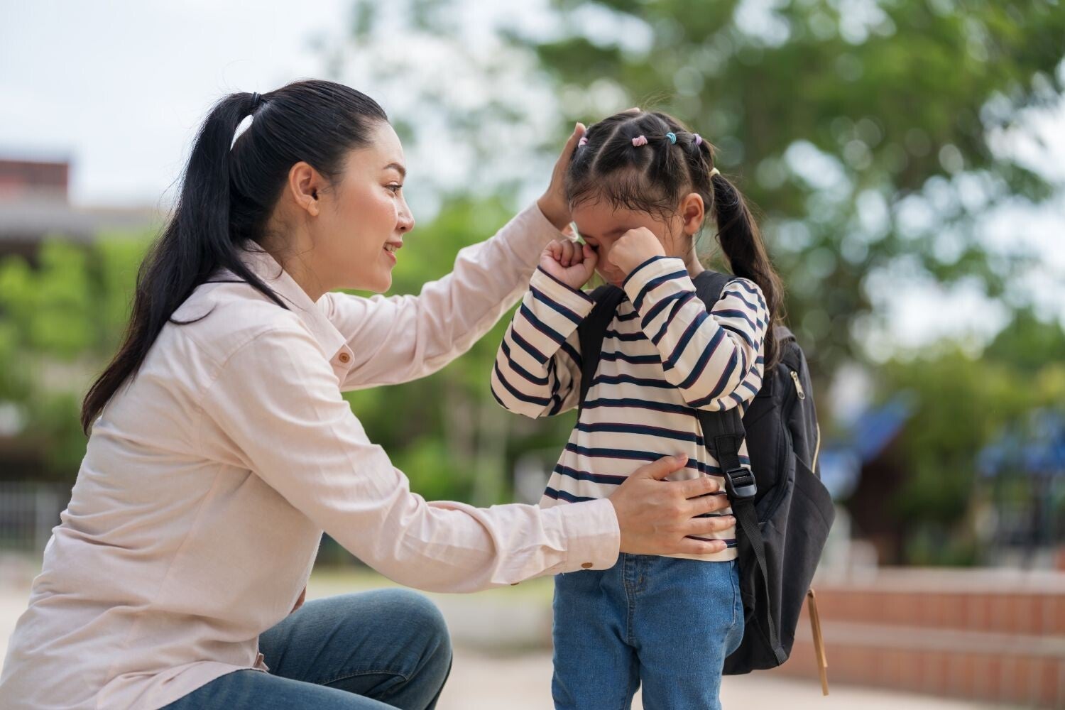 Asian mom comforts crying preschooler who doesn’t want to go to school.