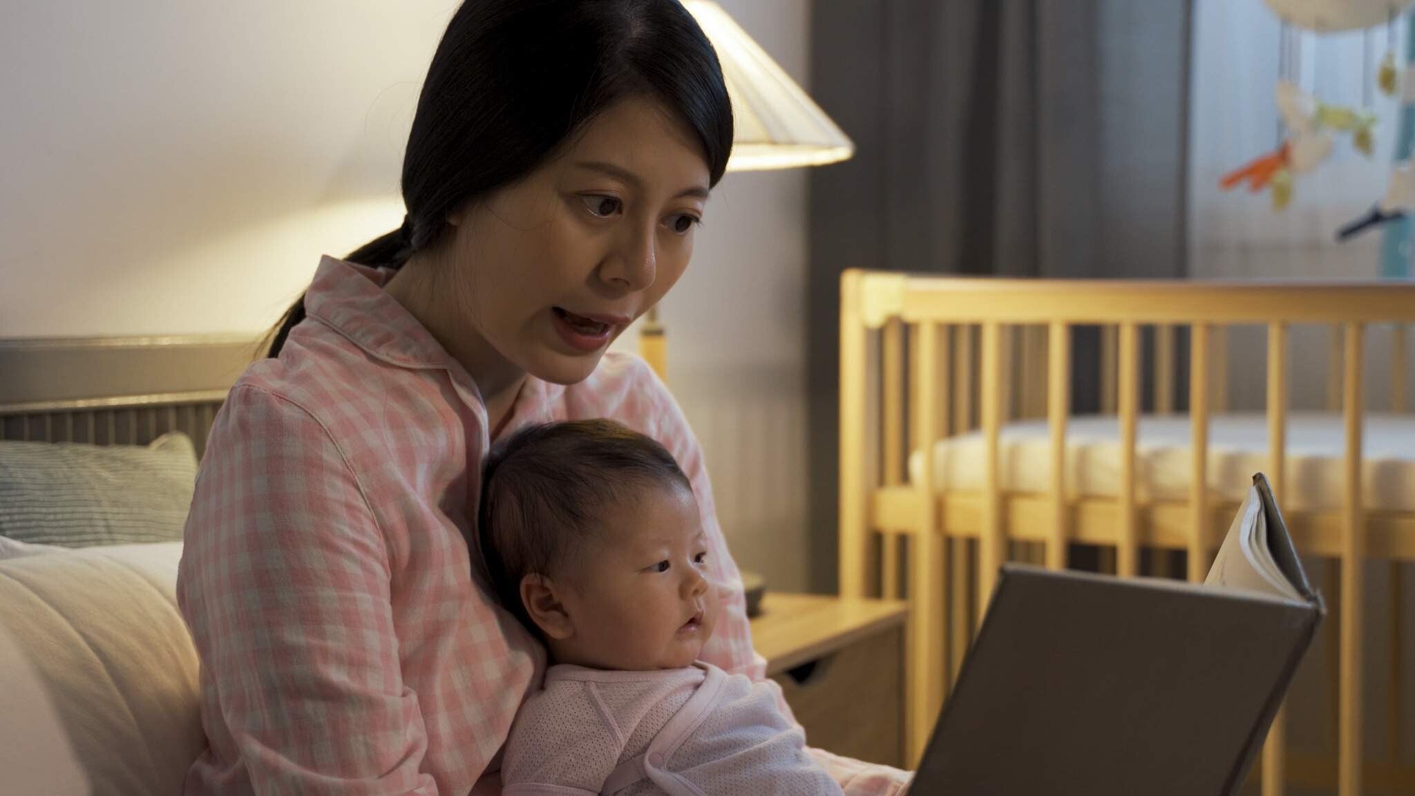 Asian mom reads a book to baby before bedtime.