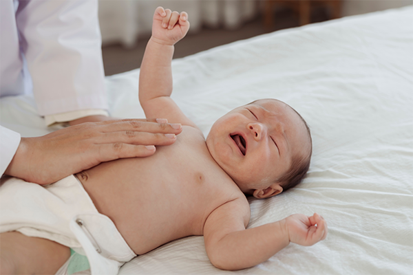 Photo of an Asian newborn crying while a doctor’s hand feels its side and tummy.