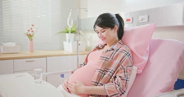 Pregnant woman holding tummy while in hospital ward.