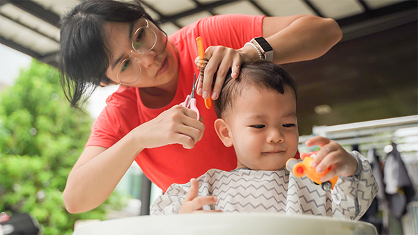 Asian toddler boy getting a haircut calmly plays with a toy.