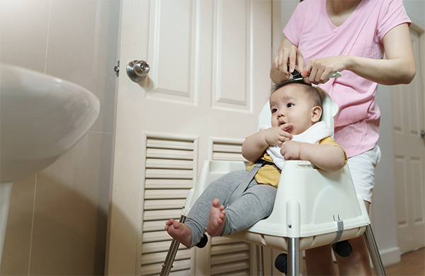 Asian toddler boy getting a pretend haircut at home.