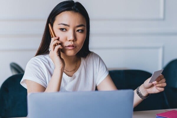 An Asian woman on the phone while holding her ID to ask how to renew it.