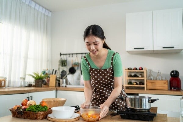 Young Asian woman putting a soupy dish on the table after cooking in the kitchen for healthy family meals.