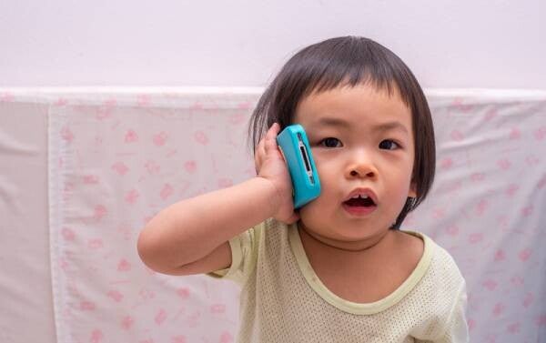 Asian 18-month-old baby girl pretends she's talking to someone on the phone.