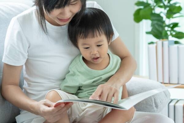 Asian 2-year-old baby boy reacts to something as his mom reads him a book.