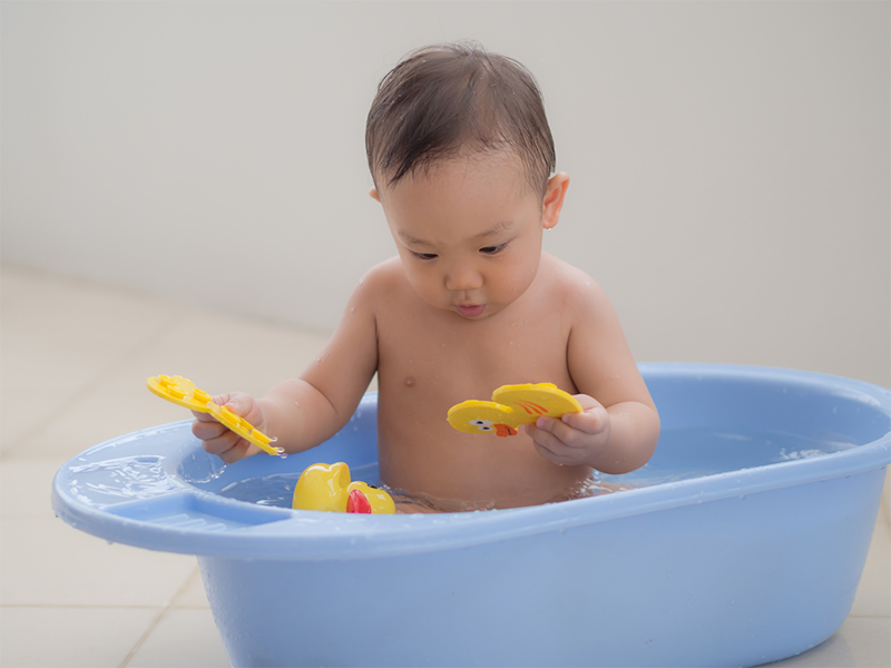 Asian baby boy plays with toys for 1-year-olds during bath time.